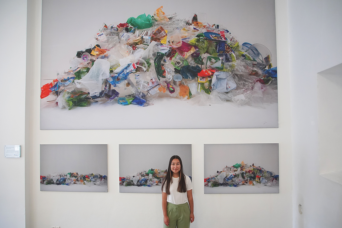 Die Gewinnerin Käthe Hohnschopp steht vor vier Leinwänden mit Plastikmülldarauf.  