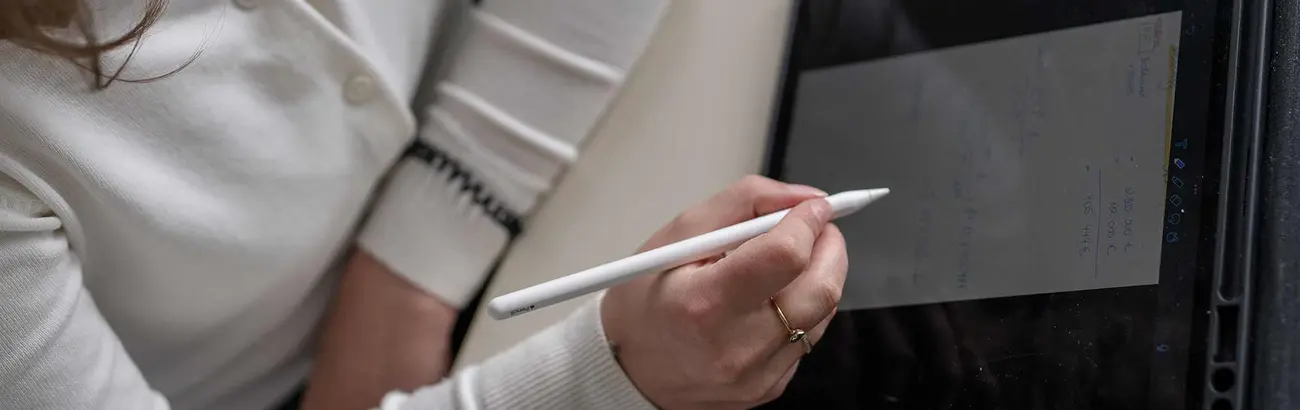 Das Bild zeigt eine Hand mit einem Stift vor einem Notizzettel. Es erinnert an eine Vorlesungssituation.