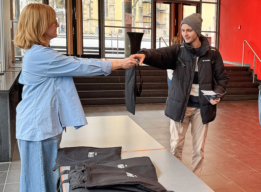 Mitarbeiterin übergibt Studenten eine Stofftasche