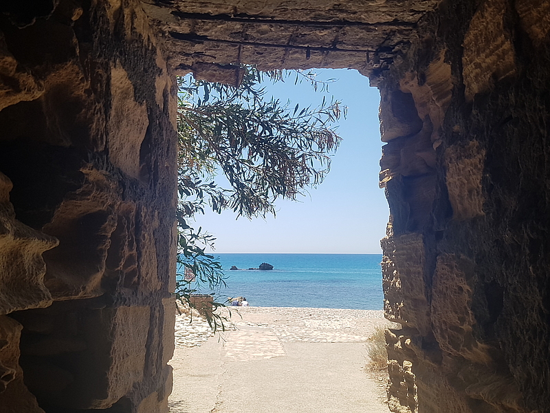 Stone gate with view of beach, sea and branch in the sunlight